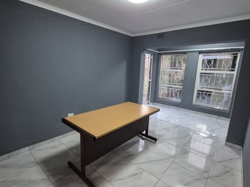 A bright, empty office space featuring modern marble-look floor tiles, dark grey walls, and security bars on the windows.