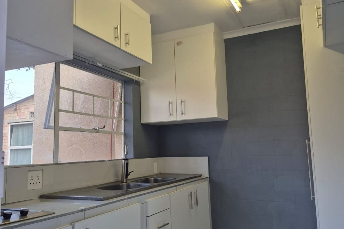 A functional kitchen featuring white built-in cabinetry, a stainless steel sink, tiled flooring, and a grey tiled feature wall.