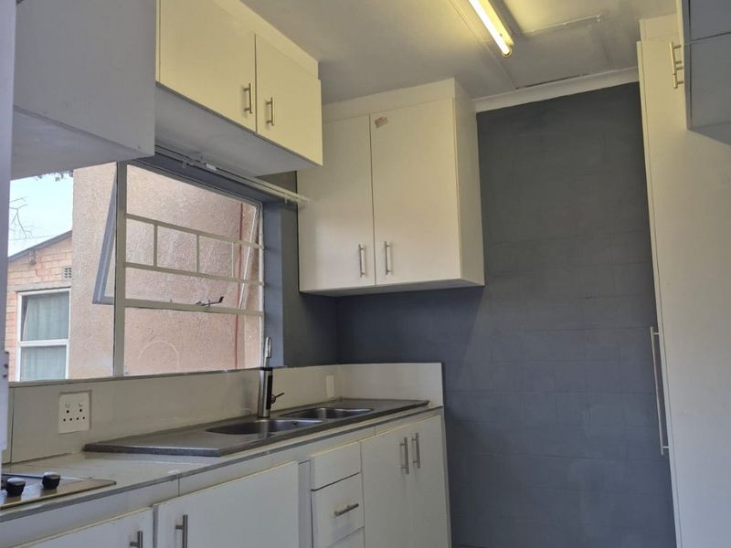 A functional kitchen featuring white built-in cabinetry, a stainless steel sink, tiled flooring, and a grey tiled feature wall.