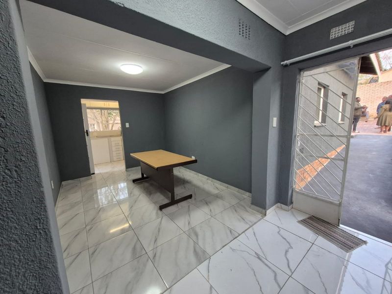 An entrance area featuring modern marble-look floor tiles, dark grey walls, and a secure metal gate leading to the exterior.