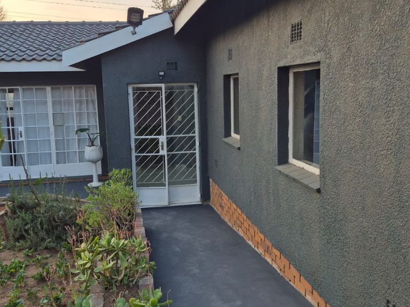 A view of the rear exterior of the house featuring a concrete pathway, security gate, and textured wall finish with brick detailing.