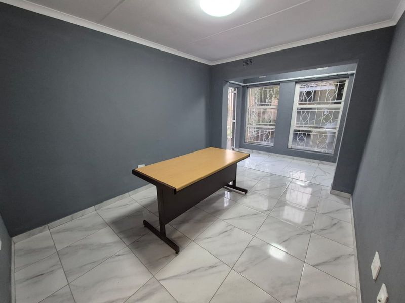 A bright, empty office space featuring modern marble-look floor tiles, dark grey walls, and secure window bars, suitable for a home workspace.