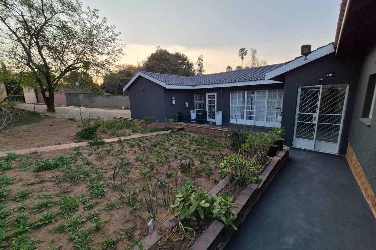 Rear view of the property featuring a dark-painted exterior, tiled roof, security gates, and a garden area with a brick retaining wall.