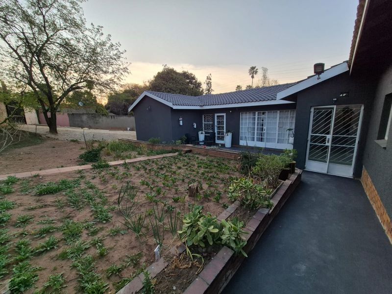 Rear view of the property featuring a dark-painted exterior, tiled roof, security gates, and a garden area with a brick retaining wall.