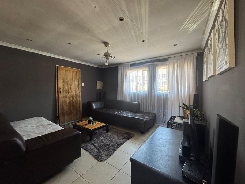 A living room featuring tiled flooring, recessed lighting, and a ceiling fan, with dark-painted walls and security bars on the windows.