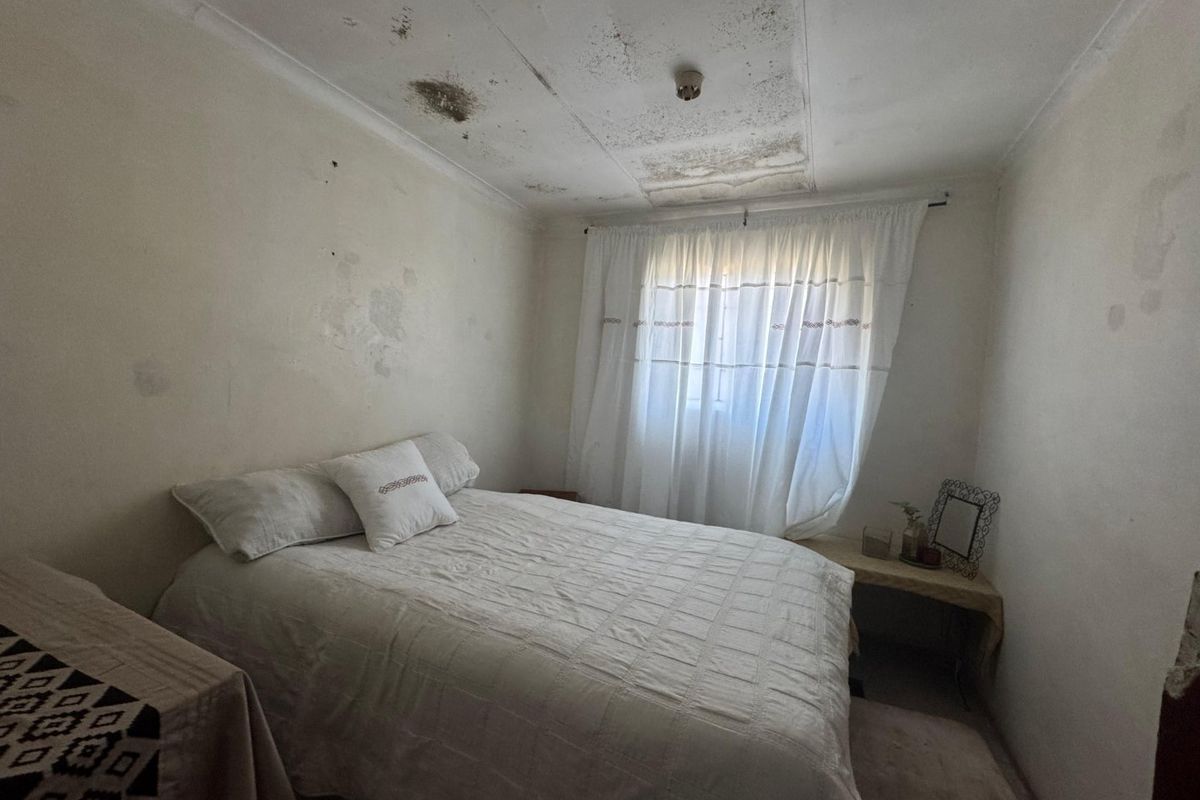 A bedroom featuring a window with curtains, requiring significant maintenance to the ceiling and walls due to visible water damage and paint deterioration.