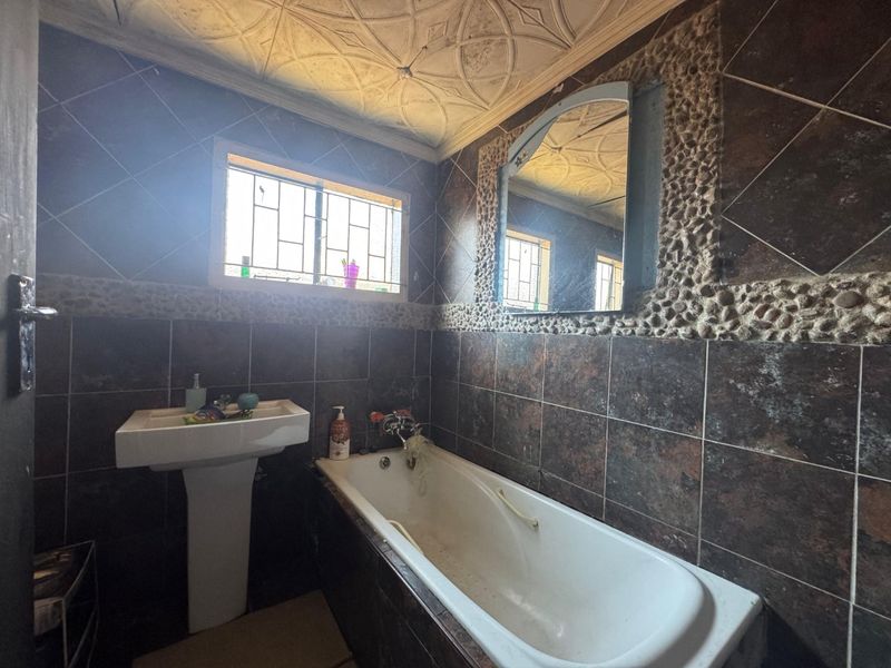 A dated bathroom featuring dark wall tiles, a pedestal basin, a bathtub, and a decorative ceiling requiring maintenance and cosmetic updates.