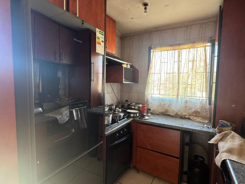 A compact kitchen featuring dark wood cabinetry, granite countertops, and a gas stove, requiring ceiling repairs and cosmetic updates to improve its overall condition.