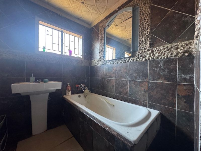 A dated bathroom featuring a built-in bathtub, pedestal basin, and dark tiled walls with decorative stone accents and a textured ceiling.