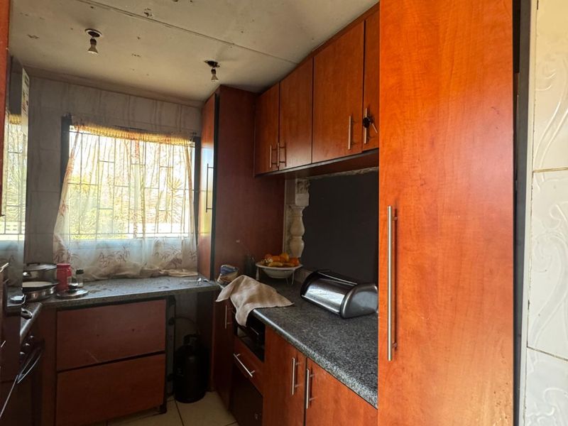 A compact kitchen featuring wood-look cabinetry, granite countertops, and tiled flooring, currently requiring ceiling repairs and general refurbishment to modernize the space.