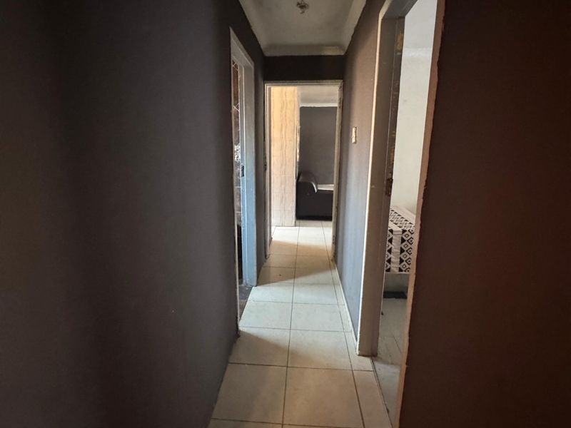 A narrow interior hallway featuring tiled flooring and dark painted walls, leading to adjacent rooms. The space requires cosmetic updates and ceiling repairs.