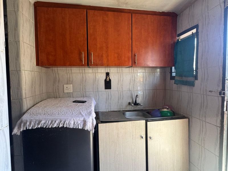 Compact laundry area featuring built-in cabinetry, a stainless steel sink, and tiled finishes, requiring some maintenance and cosmetic updates.