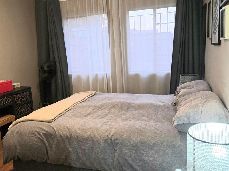 A comfortable bedroom featuring laminate flooring and windows fitted with security bars, providing a functional and private sleeping space.