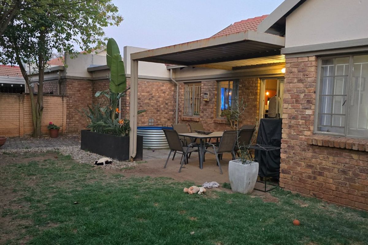 Rear exterior view of a townhouse featuring a brick facade, a covered patio area with a metal pergola, and a private garden space.