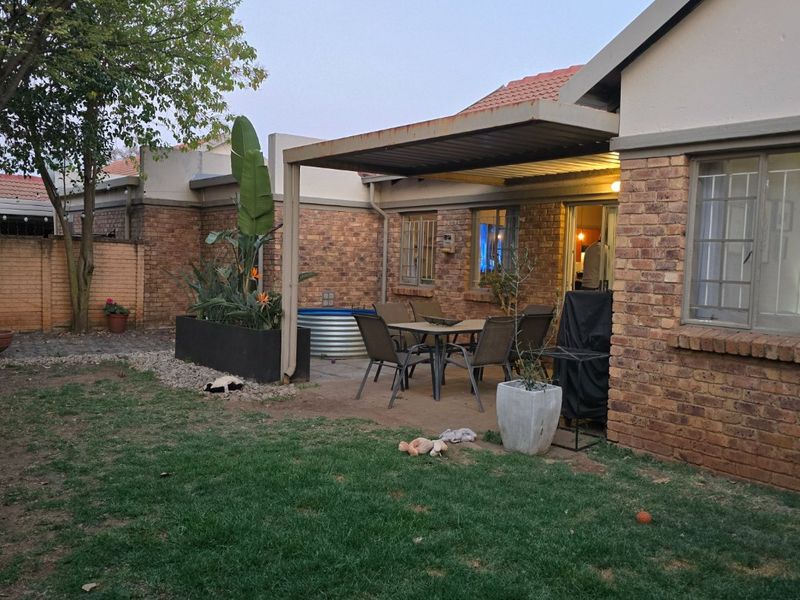 Rear exterior view of a townhouse featuring a brick facade, a covered patio area with a metal pergola, and a private garden space.