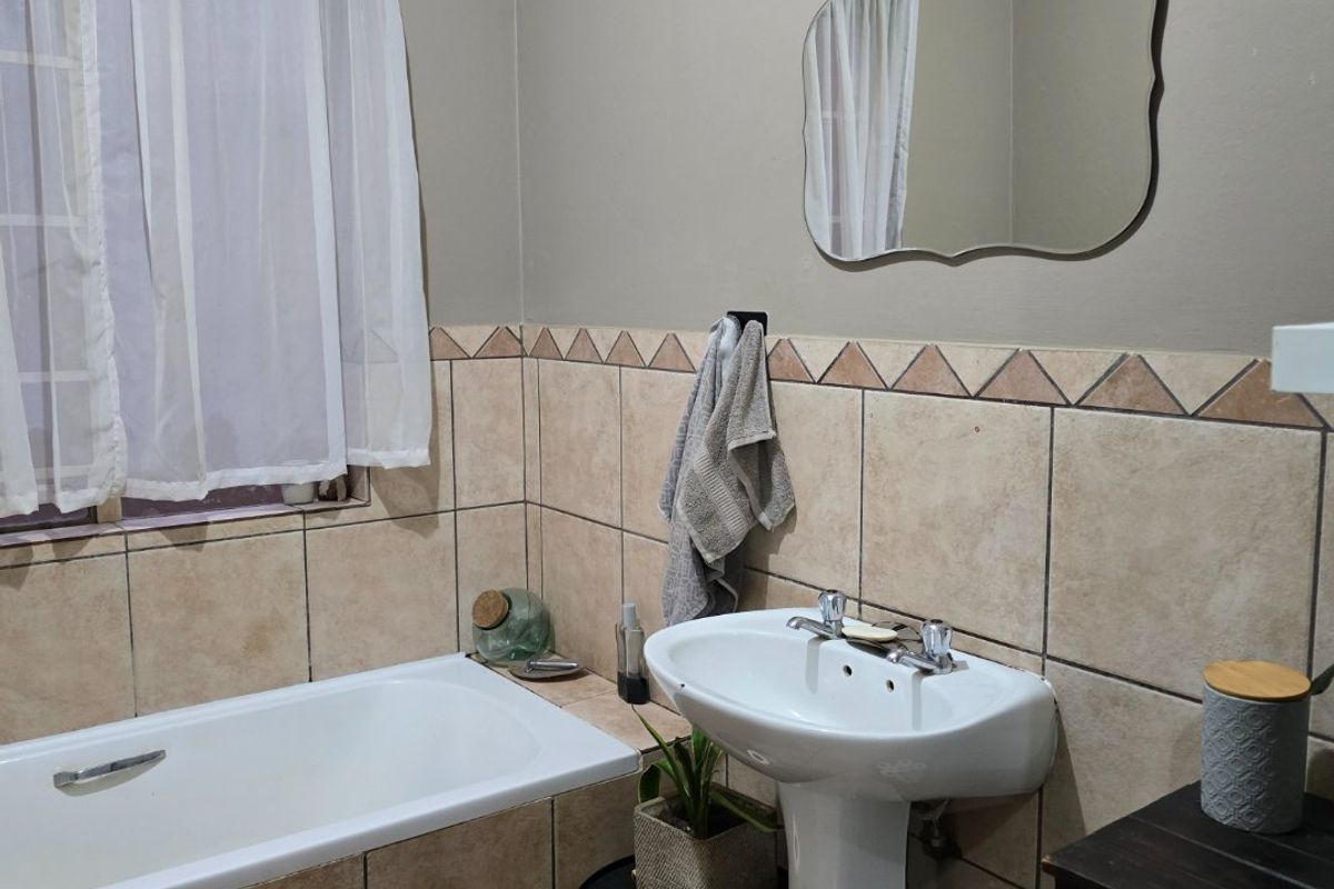 A functional bathroom featuring a pedestal basin, built-in bathtub, and neutral tiled wall finishes.
