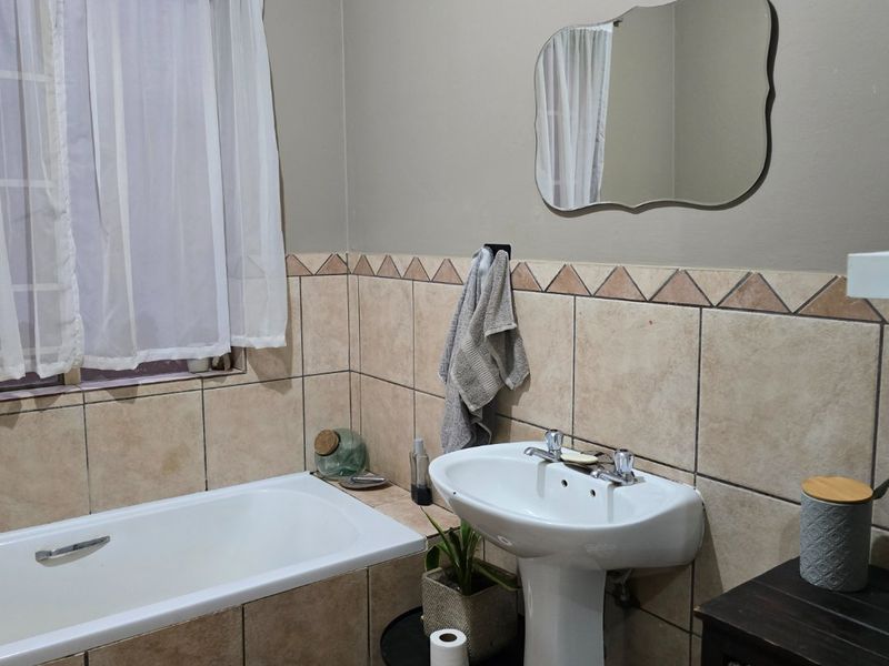 A functional bathroom featuring a pedestal basin, built-in bathtub, and neutral tiled wall finishes.