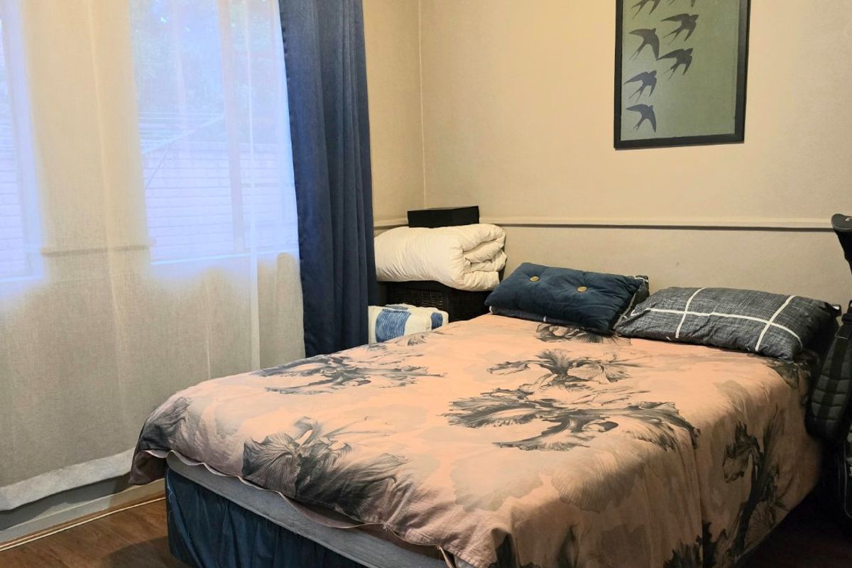 A functional bedroom featuring laminate flooring and neutral wall tones, providing a comfortable and well-lit sleeping space.