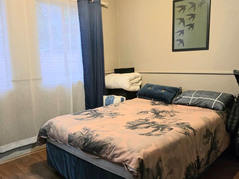 A functional bedroom featuring laminate flooring and neutral wall tones, providing a comfortable and well-lit sleeping space.