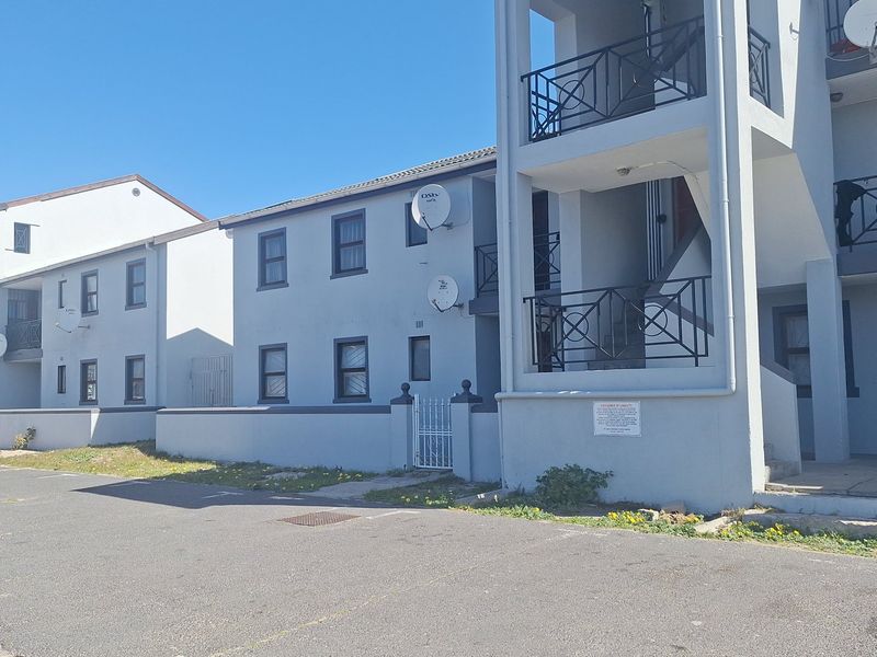 Exterior view of a multi-story apartment complex featuring balconies, external staircases, and a paved parking area.