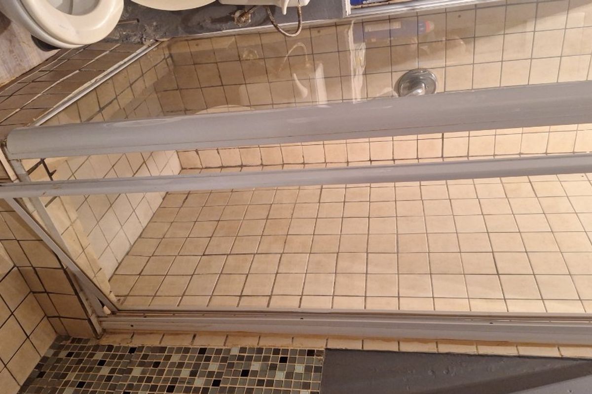 A dated bathroom featuring a tiled shower enclosure and floor, requiring cosmetic updates to the grout and fixtures to improve its overall condition.