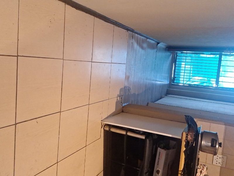 A functional kitchen area featuring tiled flooring, built-in cabinetry, and security bars on the window, requiring some maintenance and cosmetic updates.