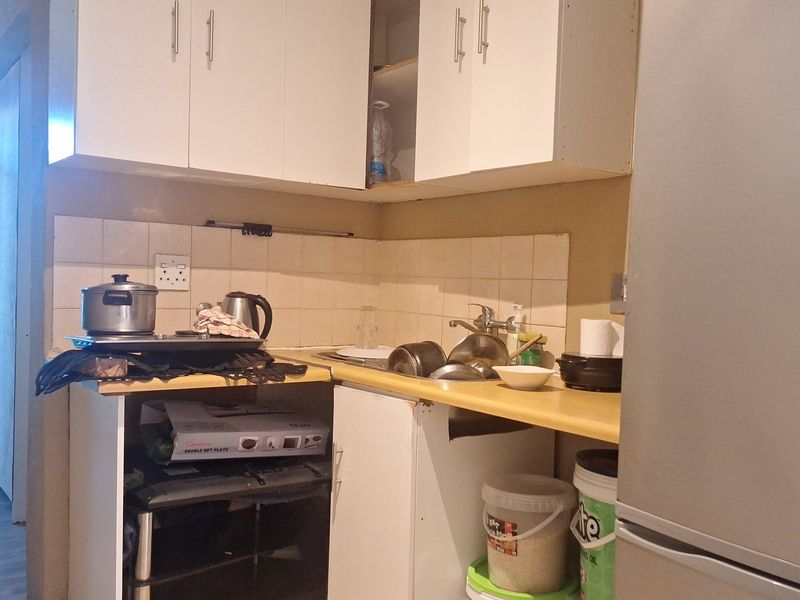 Compact kitchen area featuring upper and lower cabinetry, a tiled backsplash, and a sink, requiring some maintenance and cosmetic updates.