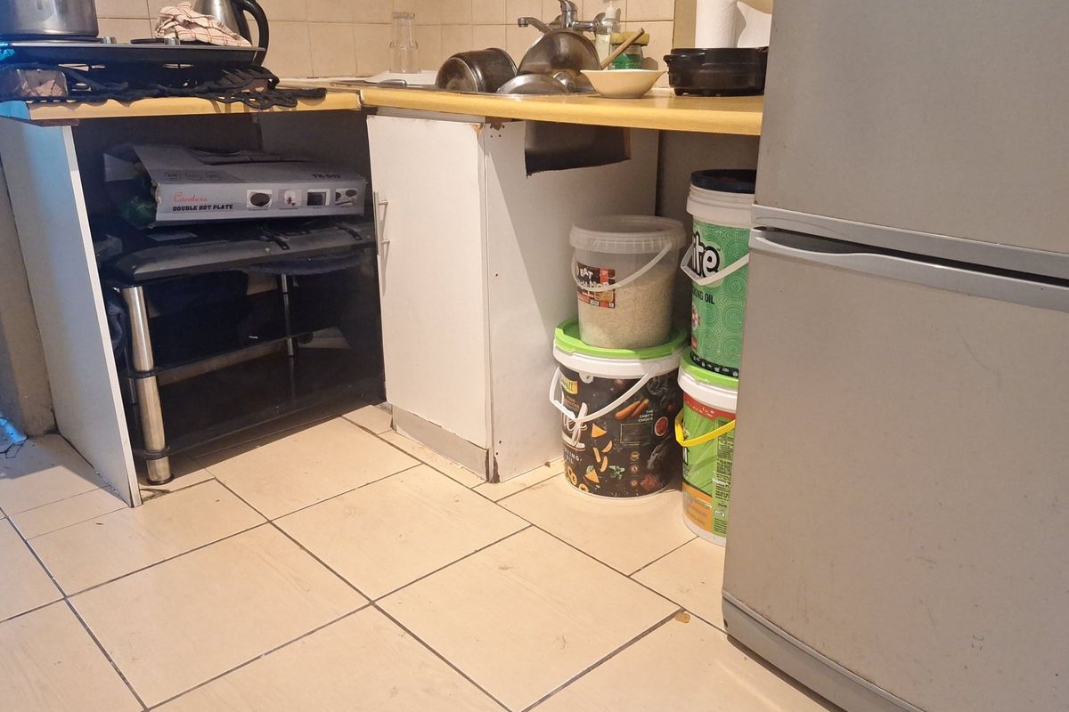 A compact kitchen area featuring basic cabinetry, a laminate countertop with a stainless steel sink, and ceramic floor tiles in need of maintenance.