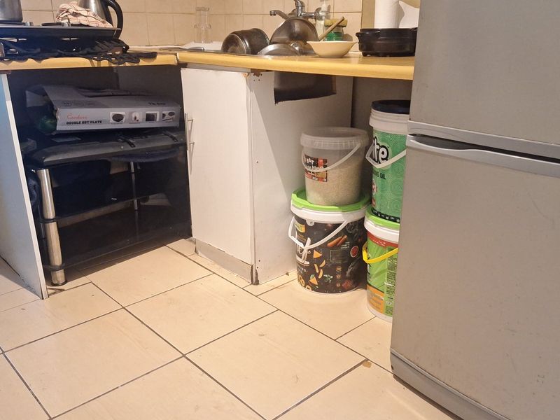 A compact kitchen area featuring basic cabinetry, a laminate countertop with a stainless steel sink, and ceramic floor tiles in need of maintenance.
