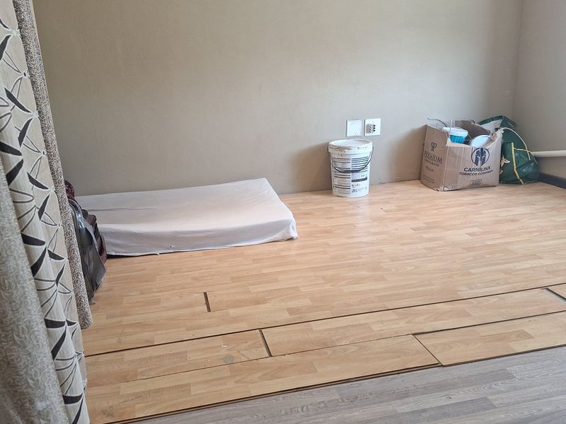 A bedroom featuring light wood-look laminate flooring with visible gaps and installation damage, requiring repair or replacement.