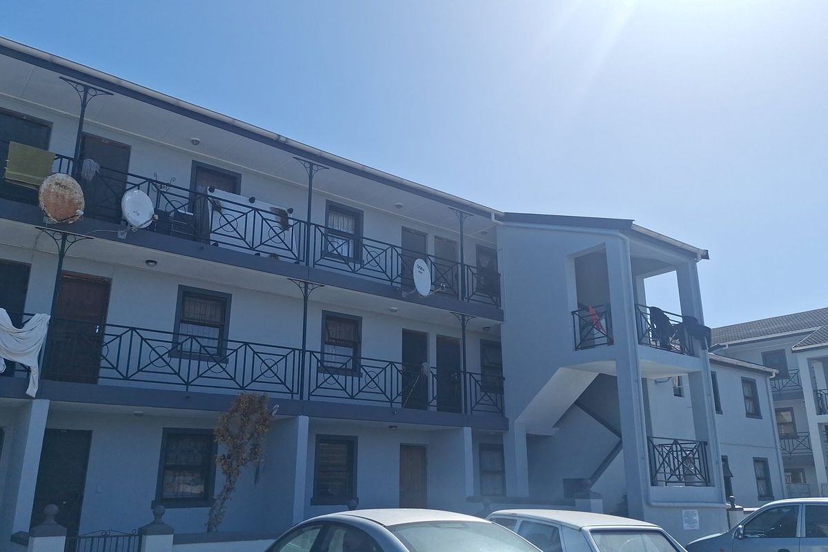 Exterior view of a multi-story apartment complex featuring concrete walkways, wrought iron balcony railings, and external stairwell access.