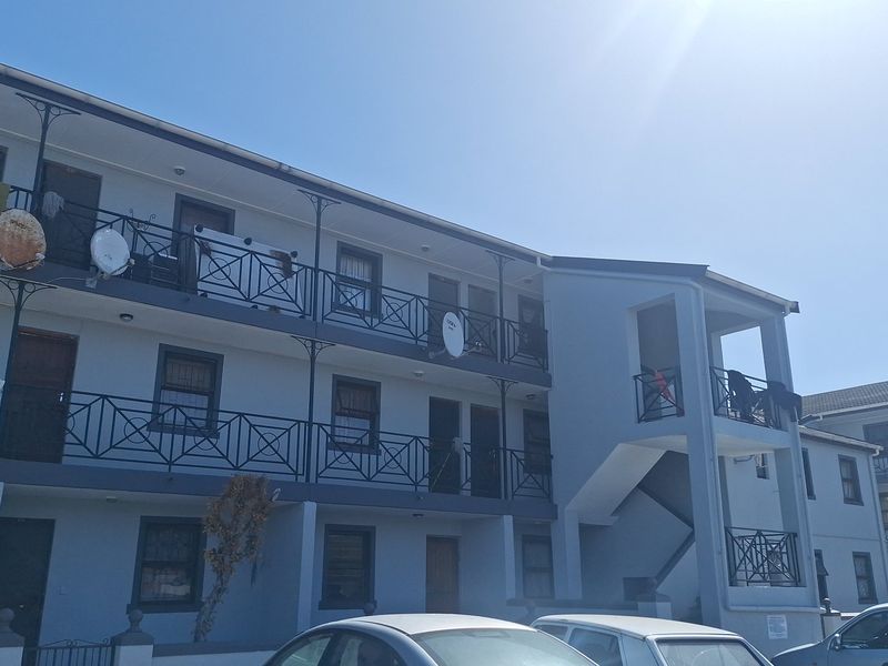 Exterior view of a multi-story apartment complex featuring concrete walkways, wrought iron balcony railings, and external stairwell access.