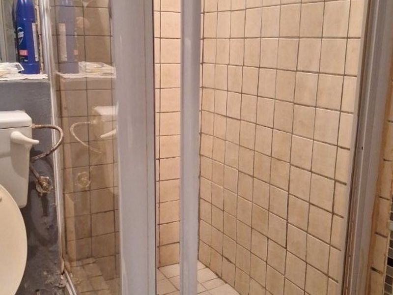 A bathroom featuring a shower enclosure with tiled walls and flooring, currently showing signs of wear and requiring maintenance or renovation.