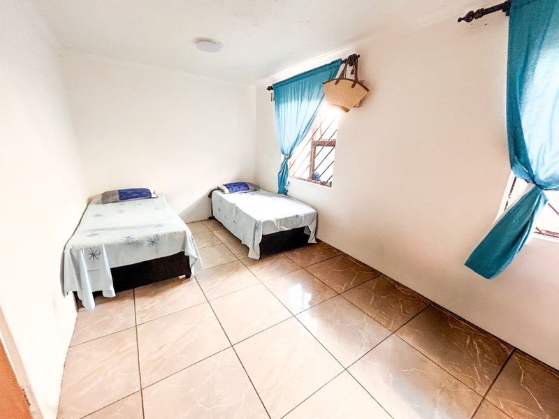 A simple bedroom featuring tiled flooring and windows fitted with security bars, providing a functional and basic living space.