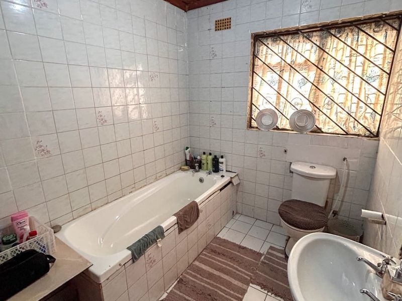 A dated bathroom featuring a built-in bathtub, pedestal basin, toilet, and tiled finishes with a timber ceiling, requiring modernization to improve aesthetic appeal.
