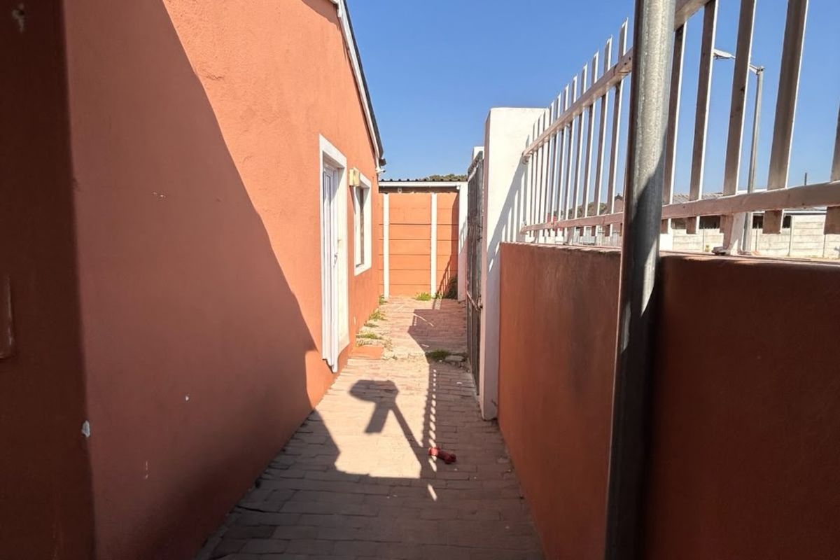 A narrow paved side passage along the exterior of the house, featuring perimeter walls with metal security fencing.