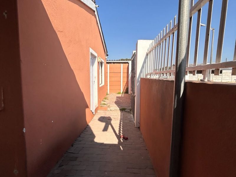 A narrow paved side passage along the exterior of the house, featuring perimeter walls with metal security fencing.