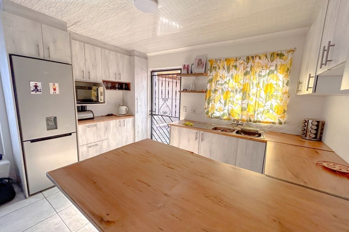 A functional kitchen featuring light wood-look cabinetry, laminate countertops, a double basin sink, and tiled flooring with direct access to the exterior.