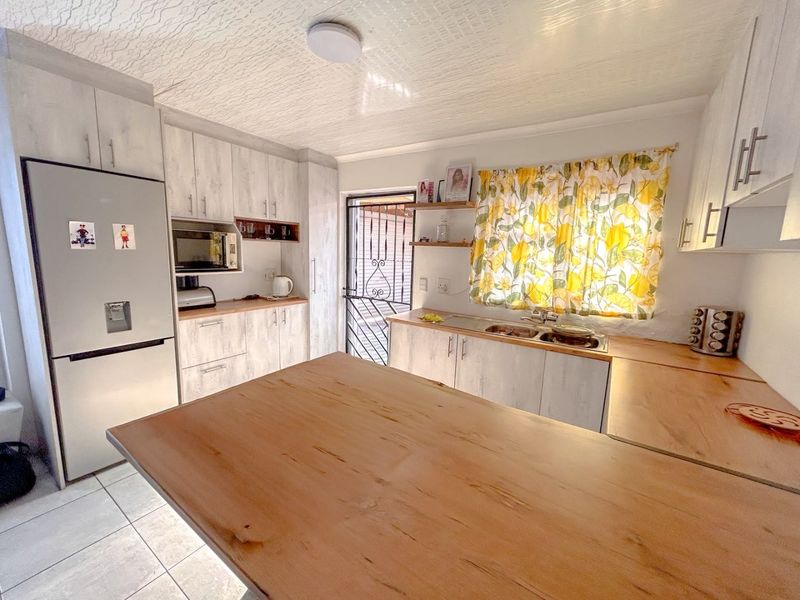 A functional kitchen featuring light wood-look cabinetry, laminate countertops, a double basin sink, and tiled flooring with direct access to the exterior.