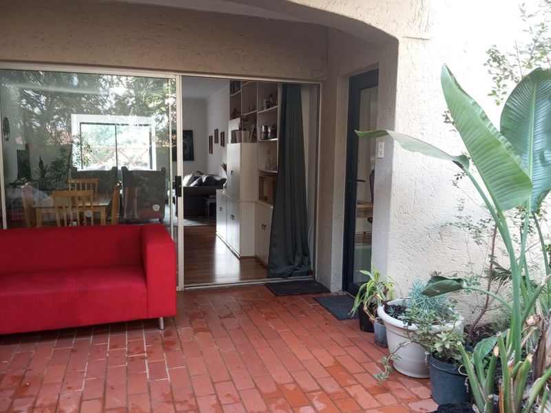 A covered patio area with brick paving, featuring a large sliding glass door providing access to the interior living space.