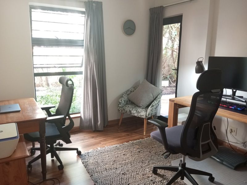 A functional home office space featuring laminate flooring, large windows for natural light, and direct access to the garden area.