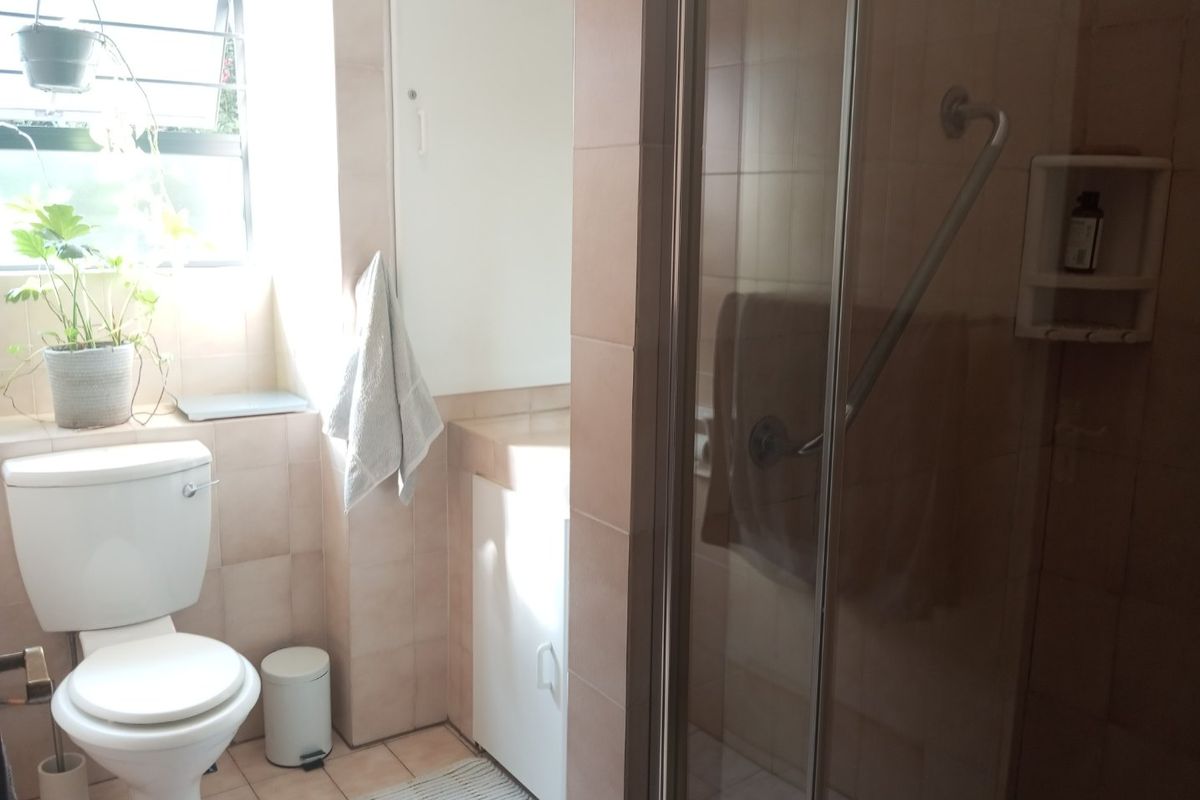 A functional bathroom featuring a shower enclosure, toilet, and vanity cabinet with neutral wall and floor tiling.