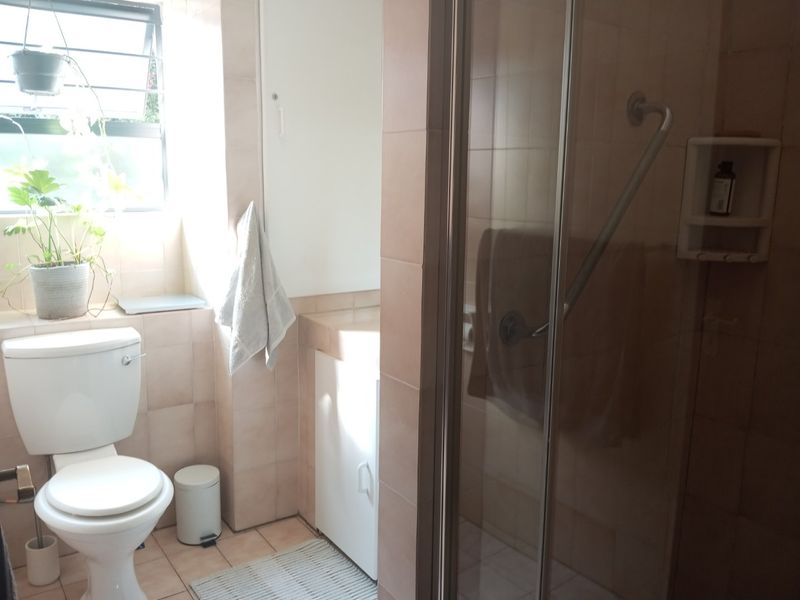 A functional bathroom featuring a shower enclosure, toilet, and vanity cabinet with neutral wall and floor tiling.