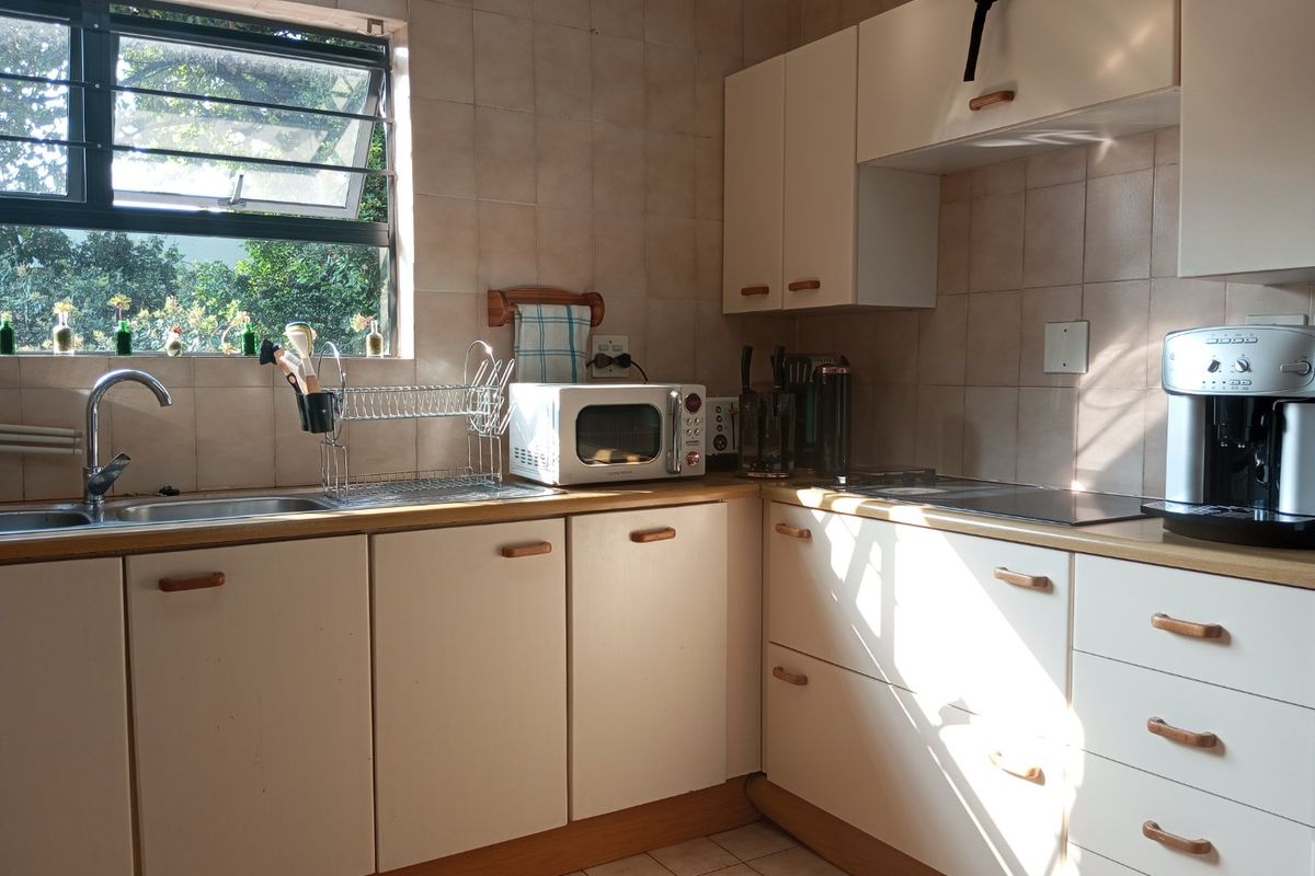 A functional kitchen featuring laminate countertops, built-in cabinetry, a stainless steel sink, and ceramic wall tiling with natural light from the window.