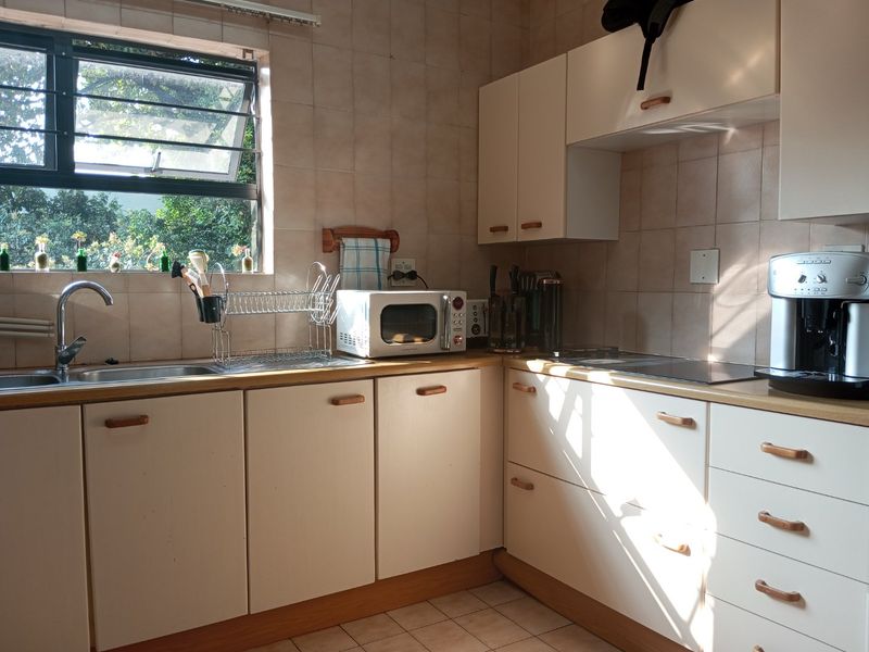 A functional kitchen featuring laminate countertops, built-in cabinetry, a stainless steel sink, and ceramic wall tiling with natural light from the window.