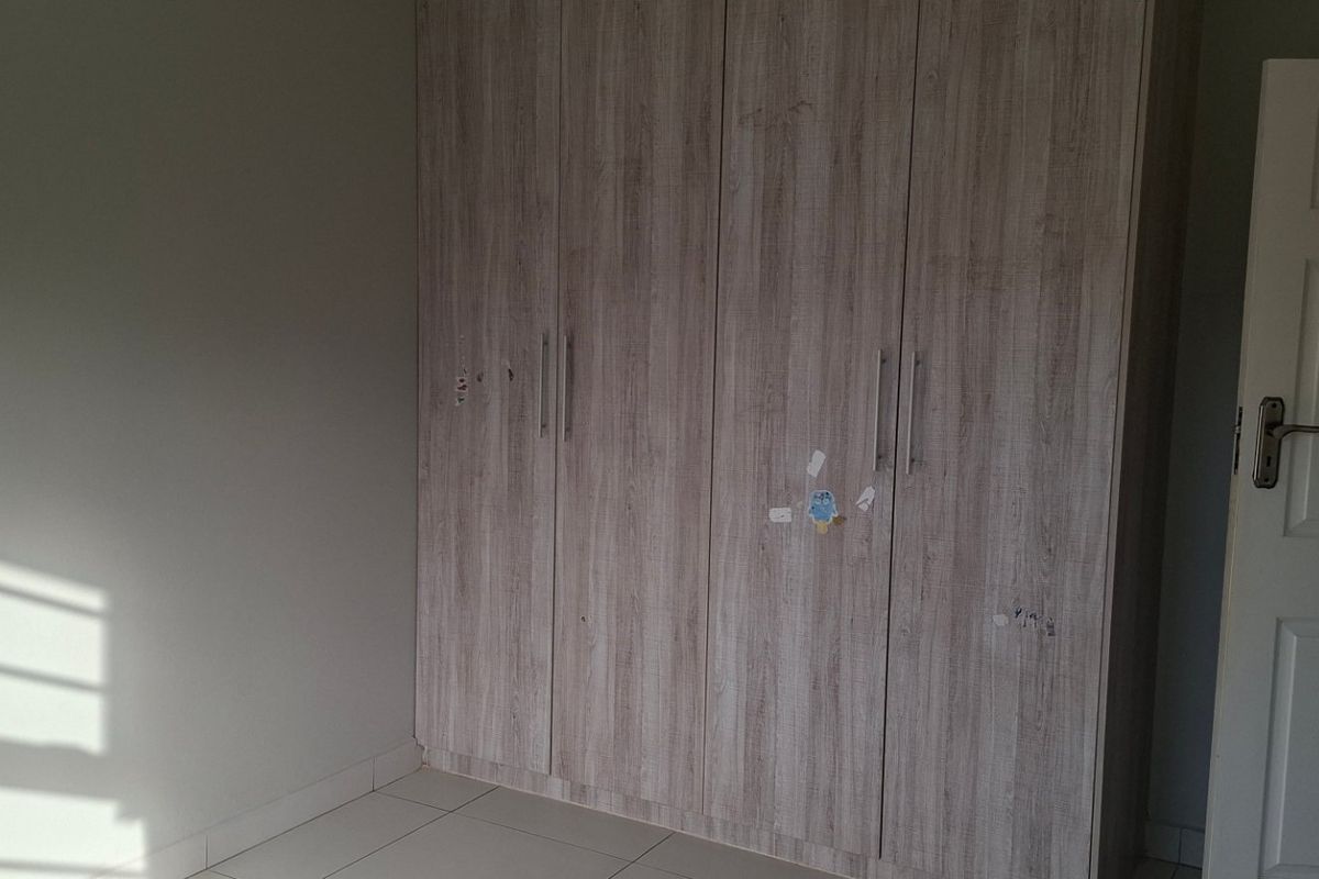 A bedroom featuring light wood-grain built-in cupboards, tiled flooring, and a classic panel door, offering a clean and functional space.