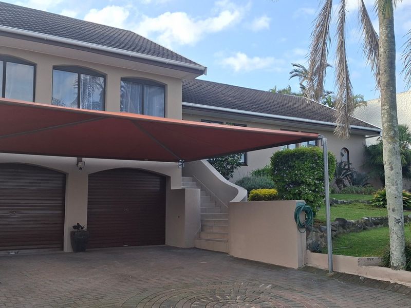 Front exterior view of a double-story house featuring a double garage, paved driveway with a shade sail, and an external staircase leading to the upper level.