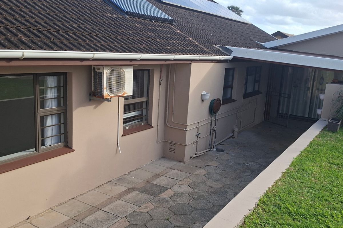 Rear exterior view of the house featuring a paved patio area, solar water heating system, and wall-mounted air conditioning unit.