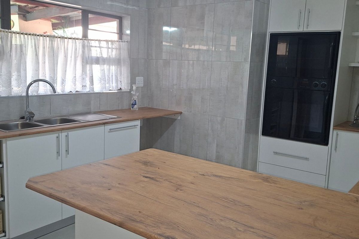 Modern kitchen featuring white cabinetry, wooden countertops, built-in oven, gas hob, and double stainless steel sink with tiled walls.