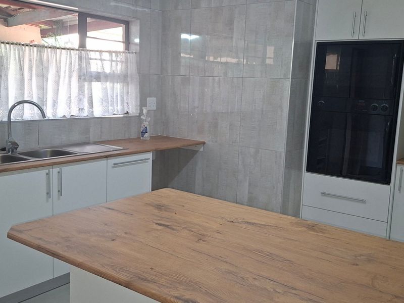 Modern kitchen featuring white cabinetry, wooden countertops, built-in oven, gas hob, and double stainless steel sink with tiled walls.